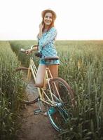 encantador joven mujer soportes en un campo con su bicicleta foto