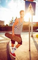 hombre en Gafas de sol con un patineta en un calle en el ciudad a puesta de sol ligero foto