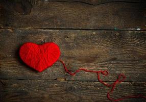 Red heart shape made from wool on old shabby wooden background photo