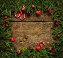 Borde de Navidad con ramas de abeto, conos, adornos navideños y bastón de caramelo sobre tablas de madera rústica foto