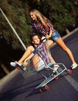 Two happy beautiful teen girls driving shopping cart outdoors photo