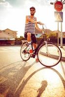 Young man in sunglasses riding a bicycle on a city street at sunset light photo