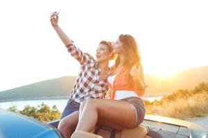 Two young beautiful girls are doing selfie in a convertible photo