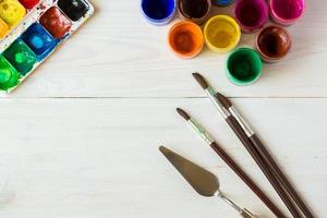 Watercolors and paint brush on white wooden background photo