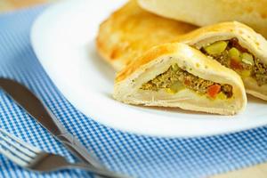 Pie stuffed with meat on a white plate and blue checkered tablecloths photo