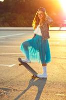 hermosa joven mujer con patineta, retroiluminado a puesta de sol foto