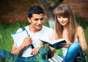 dos estudiantes chico y niña estudiando en parque en césped con libro foto