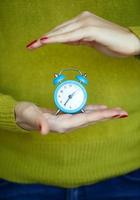 Little blue alarm clock in the hands of woman photo