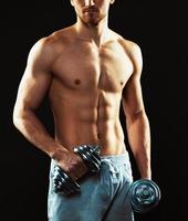 Athletic man with dumbbells on the black photo