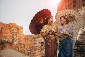 happiness face of two asian woman wearing old thai traditional suit with bamboo umbrella standing in old temple  at ayutthaya world heritage site of unesco thailand photo
