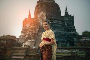 hermosa asiático mujer vistiendo tailandés tradicion vestir sonriente con felicidad en pie en contra antiguo estupa en ayutthaya mundo patrimonio sitio de la unesco cerca Bangkok Tailandia foto