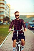 Young man in sunglasses riding a bike on city street photo
