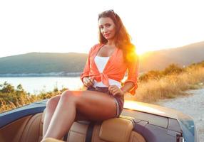 Beautiful woman sitting in cabriolet, enjoying trip on luxury modern car with open roof photo