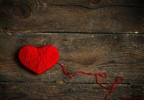 Red heart shape made from wool on old shabby wooden background photo