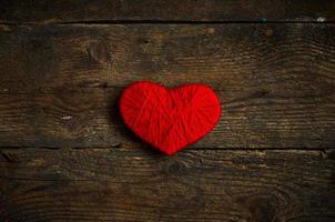 Red heart shape made from wool on old shabby wooden background photo