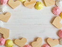 Frame made of wooden hearts and meringue pastel colors on a white wooden background photo