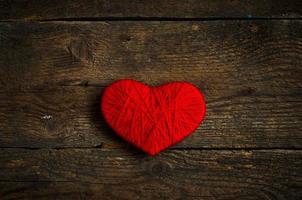 Red heart shape made from wool on old shabby wooden background photo