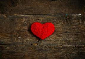 Red heart shape made from wool on old shabby wooden background photo