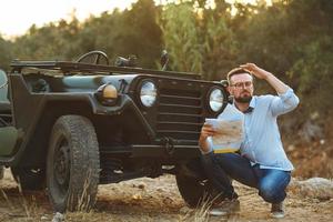 joven elegante hombre con lentes y arco Corbata ver el mapa cerca el Anticuado suv foto