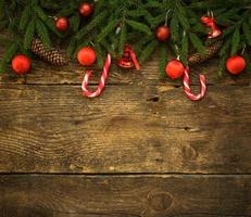 Borde de Navidad con ramas de abeto, conos, adornos navideños y bastón de caramelo sobre tablas de madera rústica foto