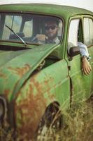 joven elegante hermoso hombre, vistiendo camisa y Gafas de sol, conducción antiguo coche foto