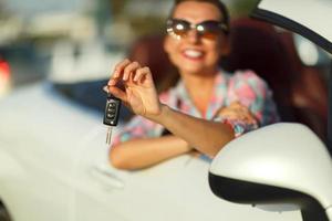 Woman sitting in a convertible car with the keys in hand - concept of buying a used car or a rental car photo