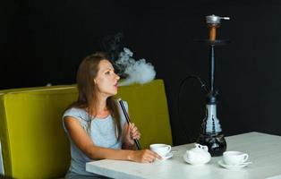 hermosa mujer de fumar un narguile y Bebiendo té en un café foto