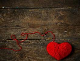 Red heart shape made from wool on old shabby wooden background photo