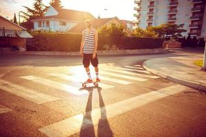 Young man in sunglasses with a skateboard on a street in the city at sunset light photo