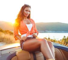 Beautiful woman sitting in cabriolet, enjoying trip on luxury modern car with open roof photo