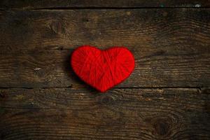 Red heart shape made from wool on old shabby wooden background photo