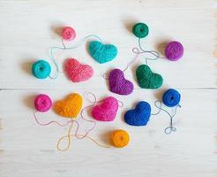 Multicolored Hearts with a balls of thread on white wooden background photo