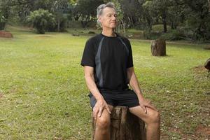 Mature Man outside at a park sitting on a tree stump relaxing before a work out photo