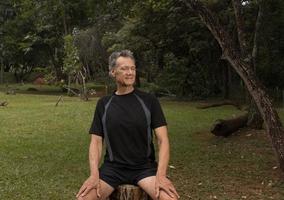 Mature Man outside at a park sitting on a tree stump relaxing before a work out photo