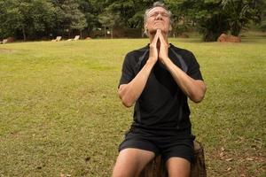 Mature Man outside at a park sitting on a tree stump stretching out his neck for pain relief photo