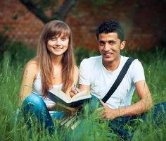 dos estudiantes chico y niña estudiando en parque en césped con libro foto