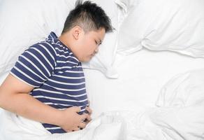 Top view of asian child suffering from stomachache and lying on bed. photo