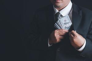 Man putting bribe money into pocket on black background, photo