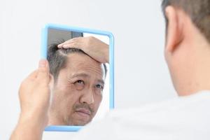 Asian middle-aged man was looking in the mirror and was worried about the many facial wrinkles photo