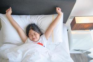 Cute little girl stretching her arms happily from waking up in her bed. photo