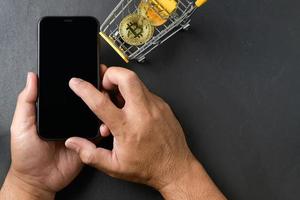 male hands using smartphone for sell or buy  virtual money, bit coin in yellow trolley on black background photo