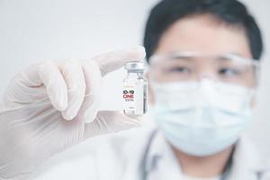 Development and creation of a coronavirus vaccine COVID-19. Young doctor with a stethoscope holding COVID-19 vaccine on white background. photo