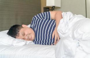 asian fat child suffering from stomachache and lying on bed. photo