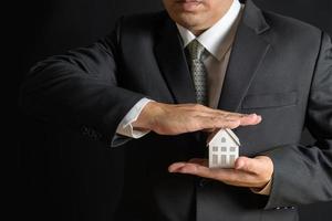 Paper house is covered by business man hands of a real estate agent to protect the house for customers, photo