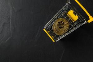 bit coin in yellow trolley on black background and top view, electronic virtual money for web banking and international network payment photo