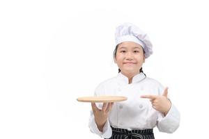 cute girl chef holds wooden plate and points her finger at plate. food menu presentation photo