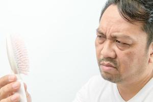 Middle-aged man looking at comb brush with loss hair and stressed about his hair loss problems photo