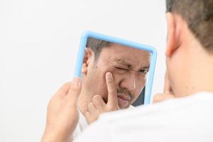 A middle-aged man looking in the mirror and worried about blemishes and wrinkles on his face photo