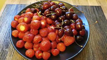 On a black plate, washed strawberries and cherries. photo