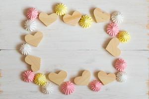 Frame made of wooden hearts and meringue pastel colors on a white wooden background photo